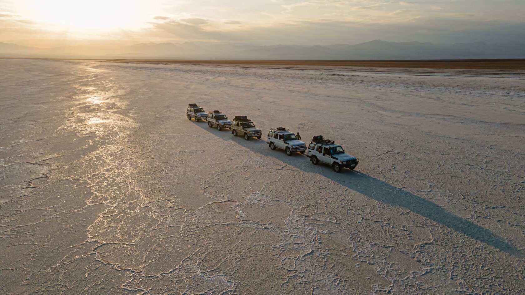 Vehicle convoy crossing the salt flats at sunrise
